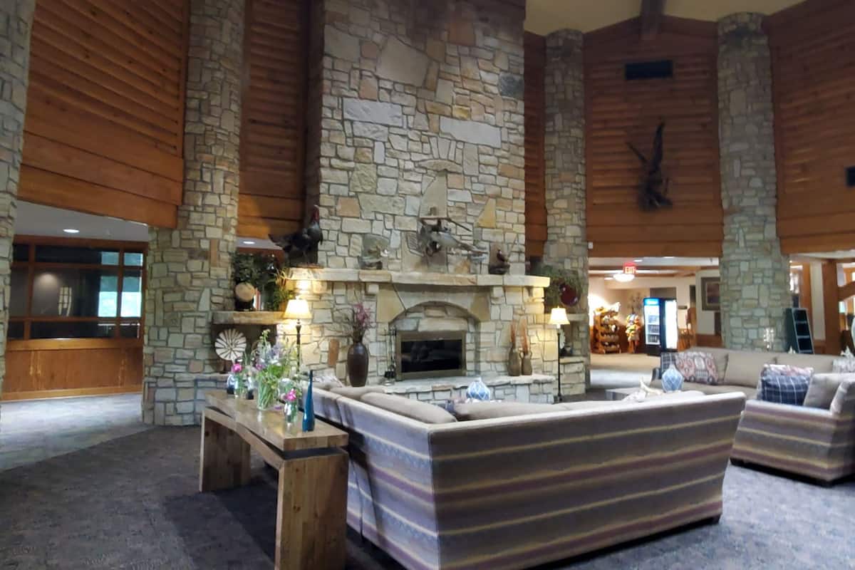 A spacious lobby with a stone fireplace, wooden beams, and a seating area with striped sofas.