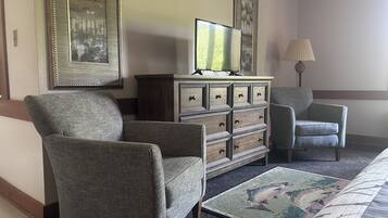 A hotel room with a large bed, two armchairs, a wooden dresser, and two framed pictures on the wall.