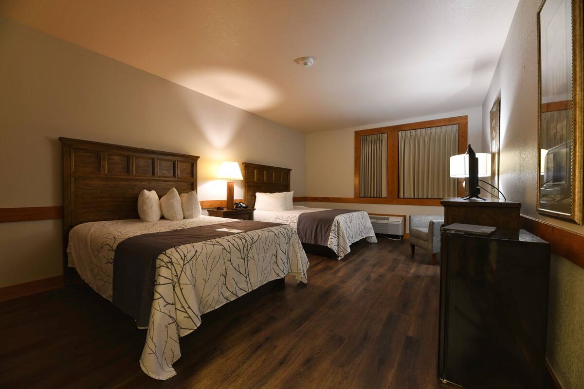 A hotel room with two beds, a desk, a refrigerator, and a large mirror.