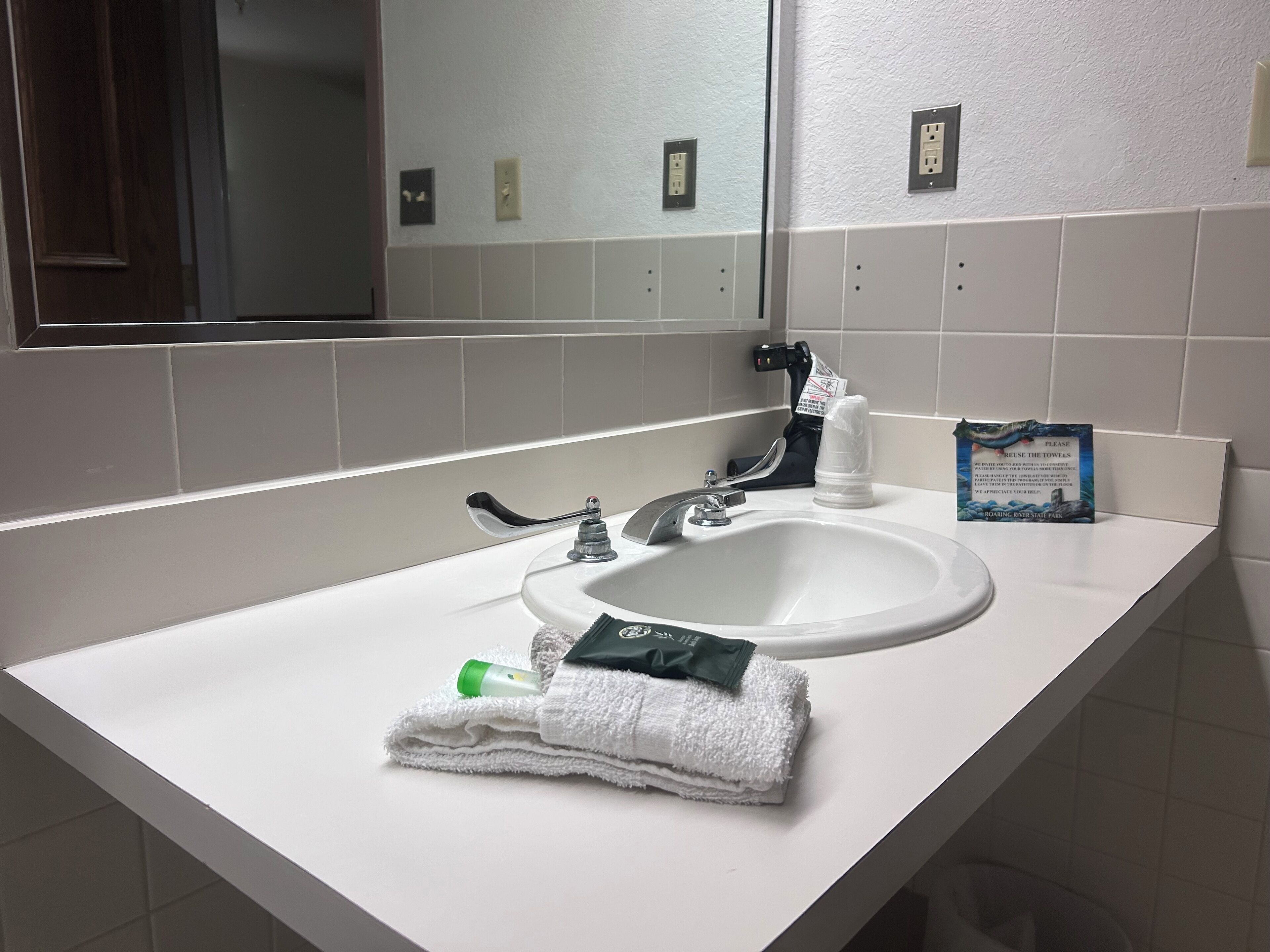A bathroom with a white sink, a mirror, and a towel dispenser.