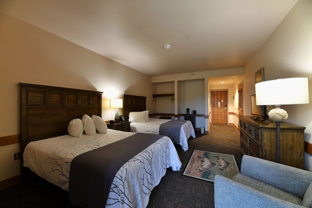 A hotel room with two beds, a desk, a chair, a lamp, and a painting on the wall.