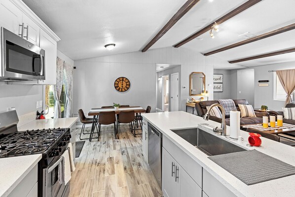 Una cocina moderna con una isla central, un comedor y una sala de estar con sofá y mesa de centro.