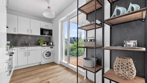 Et moderne køkken med hvide skabe, en vaskemaskine og et stort vindue med udsigt til en balkon.