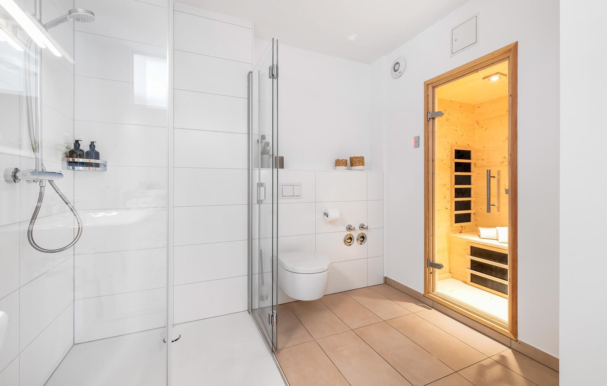 A modern bathroom with a glass shower enclosure, a toilet, and a wooden sauna door.