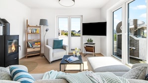 A modern living room with a fireplace, a bookshelf, a comfortable sofa, a coffee table, and a large window offering a view of the outside.