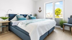 A modern bedroom with a large bed, a bedside table, a chair, and a view of the outside.