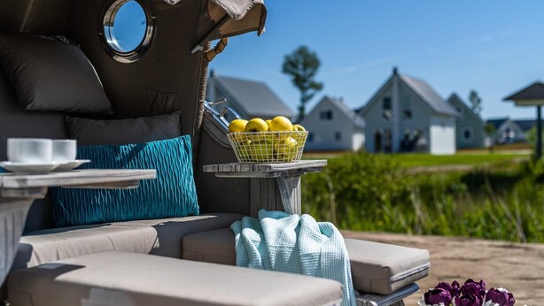 A cozy outdoor seating area with a cushioned sofa, a small table with a basket of lemons, and a view of houses in the background.