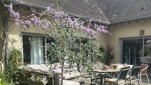 Ein Patio mit Tisch und Stühlen, umgeben von Topfpflanzen und einem kleinen Garten.