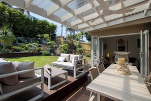 Un patio cubierto con mobiliario exterior, una mesa con una vela y vistas a un jardín y un patio trasero.