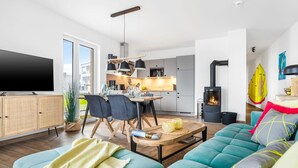 A modern living room with a sofa, a TV, and a dining area with chairs and a table. - Cozy apartment in Olpenitz with sauna (Olpenitz)