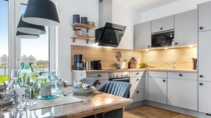 A modern kitchen with a dining area, featuring a wooden table, chairs, and a view of the outside. - Cozy apartment in Olpenitz with sauna (Olpenitz)