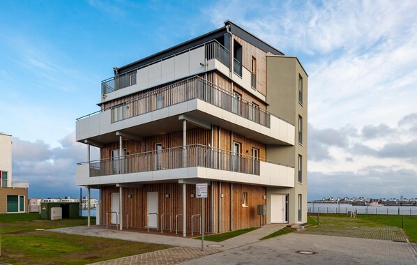 Un immeuble moderne à plusieurs étages, doté de balcons, d’un toit plat et offrant une vue sur l’eau.