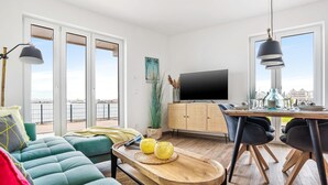 A modern living room with a sofa, a dining table with chairs, a TV, and a view of the outside. - Cozy apartment in Olpenitz with sauna (Olpenitz)