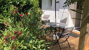 Eine Terrasse mit Tisch und Stühlen, umgeben von üppiger Bepflanzung und einem weißen Zaun.