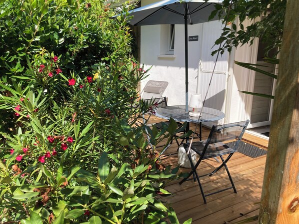 En terrasse med et bord og stole, omgivet af frodigt grønt og et hvidt hegn.