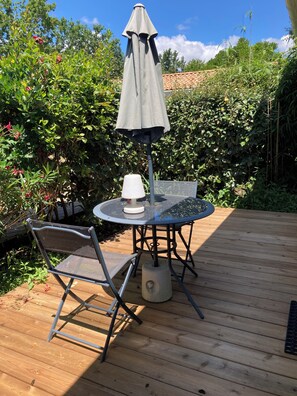 En træterrasse med et rundt bord, en stol, en parasol og en lampe.