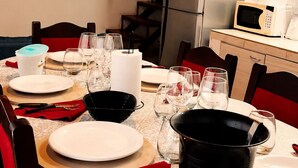 Un comedor con una mesa dispuesta para cuatro, un televisor mostrando 'NETFLIX', un refrigerador y un microondas al fondo.