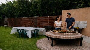 Una parrilla de ladrillo circular con comida, una mesa con sillas y una cerca de madera en un patio trasero.