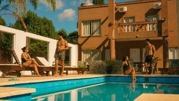 A swimming pool area with lounge chairs, a building with a balcony, and a clear sky.