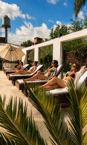 A poolside area with lounge chairs, a water tank, and a pergola with a view of the sky and greenery.