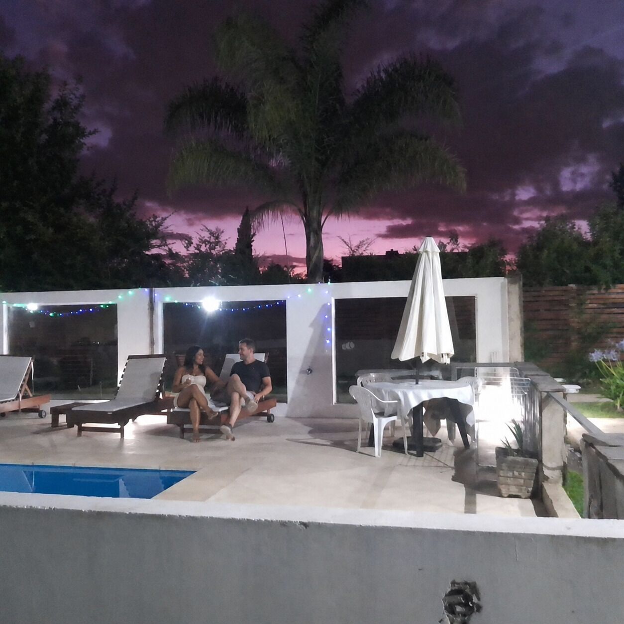 Un área de piscina al aire libre con sillas de descanso, una mesa y sombrillas.