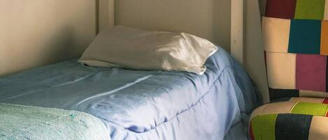 Una cama literera con una manta azul, un almohadón blanco y una silla colorida.
