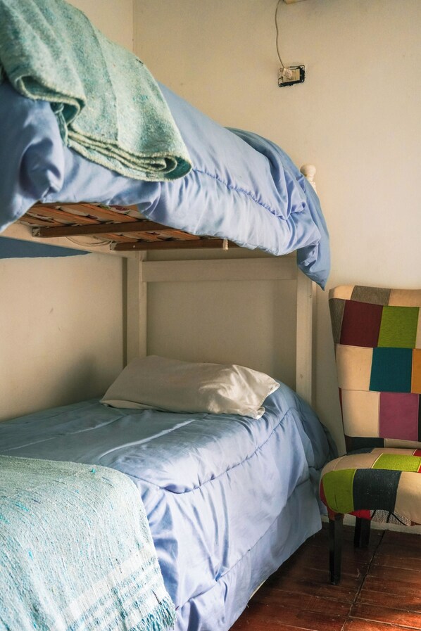 A bunk bed with a blue blanket, a white pillow, and a colorful chair.