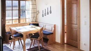 Et spiseområde med et træbord og stole, en bænk og udsigt gennem et vindue med gardin.