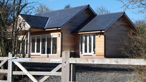 A wooden cabin with a sloped roof, large windows, and a wooden gate in front.