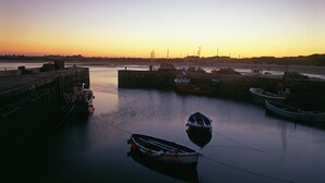 A harbor with boats docked, calm water, and a sunset in the background.
