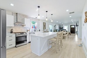 Une cuisine moderne avec des meubles blancs, un îlot central et des luminaires suspendus.