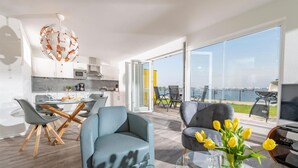 Ein modernes Wohnzimmer mit Essbereich, einer Küche und einem Balkon mit Meerblick.