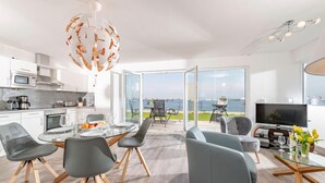 Ein modernes Wohnzimmer mit Essbereich, einer Küche und einem großen Balkon mit Meerblick.