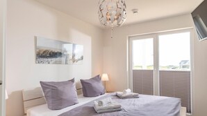 Ein Schlafzimmer mit einem Bett, Kissen, einer Lampe, einem Bild und Blick durch das Fenster.
