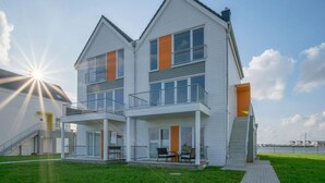 Ein zweigeschossiges Wohngebäude mit Balkon, überdachter Veranda und Blick auf das Wasser.
