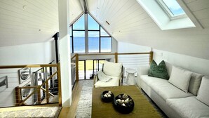 A spacious loft bedroom with a large skylight, a white sofa, and a view of the sea. - Zen Oceanfront Chalet- Hot Tub & Sauna -  Private (South Shore)