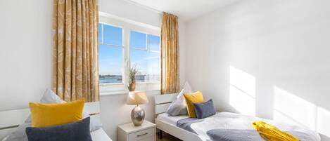 A modern bedroom with two beds, a bedside table, a lamp, and a window with curtains.