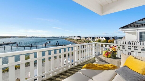 Un balcon avec vue sur la mer, une clôture blanche et un canapé avec des coussins.