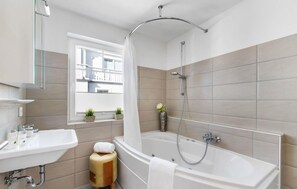 Un baño moderno con bañera, ducha y lavamanos. Hay una ventana con plantas en el alféizar.