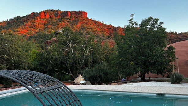 A pool with a wicker chair, a tent, and a view of a red rock mountain.