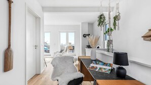 Un salon moderne avec un plancher en bois, un fauteuil blanc et moelleux, une table à manger avec des magazines et des plantes suspendues.