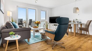 A modern living room with a sofa, a blue armchair, a dining table, and a TV. - Nice apartment in Olpenitz with WiFi (Olpenitz)
