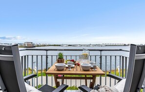 A dining table with bowls, cups, and a pitcher, set on a balcony with a view of a waterfront and buildings in the background. - Nice apartment in Olpenitz with WiFi (Olpenitz)