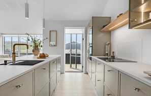 A modern kitchen with a central island, a large window, and a view of a building outside. - 3 bedroom lovely home in Løkken (Løkken)