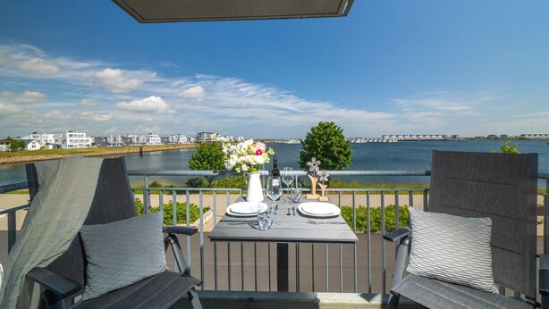 A dining table set for two with a view of the water and buildings in the background. - Cozy apartment in Olpenitz (Olpenitz)
