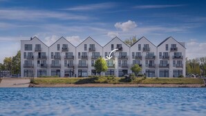 A modern multi-story residential building with balconies, located near a body of water. - Cozy apartment in Olpenitz (Olpenitz)
