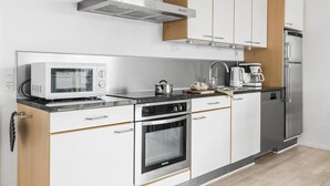 Una cuina moderna amb electrodomèstics d'acer inoxidable, armaris de fusta i forn integrat.