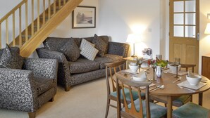 A living room with a wooden staircase, patterned sofas, a dining table with chairs, and a door with glass panels. - Lovely property with an open staircase leading to 2 bedrooms and a bathroom. (Ellington, near Druridge)