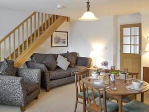 A living room with a wooden staircase, patterned sofas, a dining table with chairs, and a door with glass panels. - Lovely property with an open staircase leading to 2 bedrooms and a bathroom. (Ellington, near Druridge)