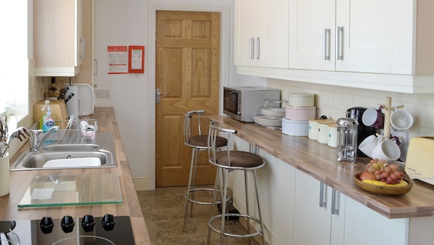 Een moderne keuken met een houten deur, witte kasten, een roestvrijstalen spoelbak, een magnetron en een fruitschaal op het aanrecht.